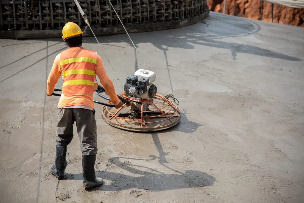 Construction worker wear standard safety uniform pouring and leveling fresh concrete at construction site